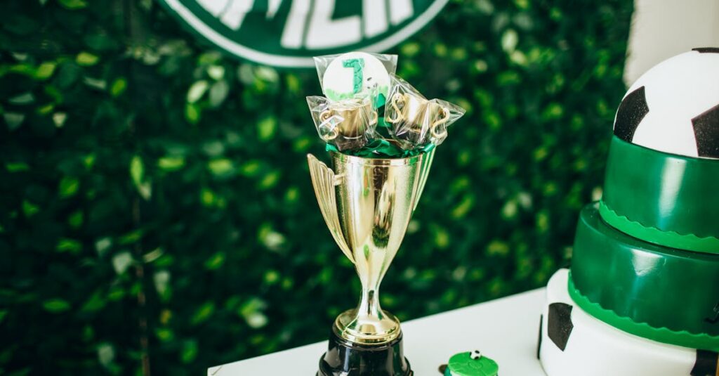 A golden trophy on a decorated table with soccer-themed cake and greenery backdrop.